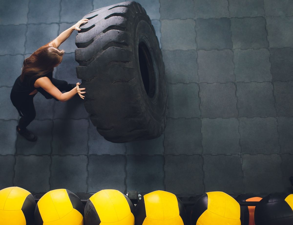 Fit female athlete working out with a huge tire, turning and carry in the gym. woman exercising with big tire.